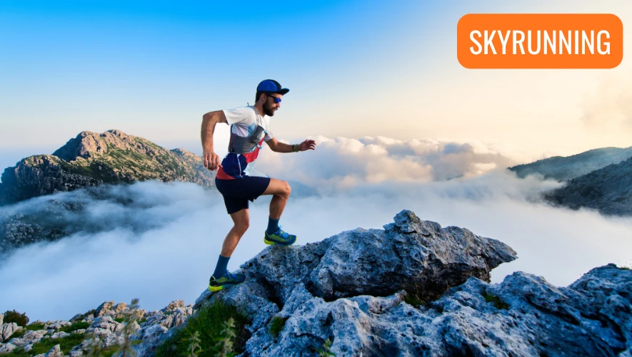 En löpare springer på mycket hög höjd (skyrunning) och flera bergstoppar syns sticka upp ur moln